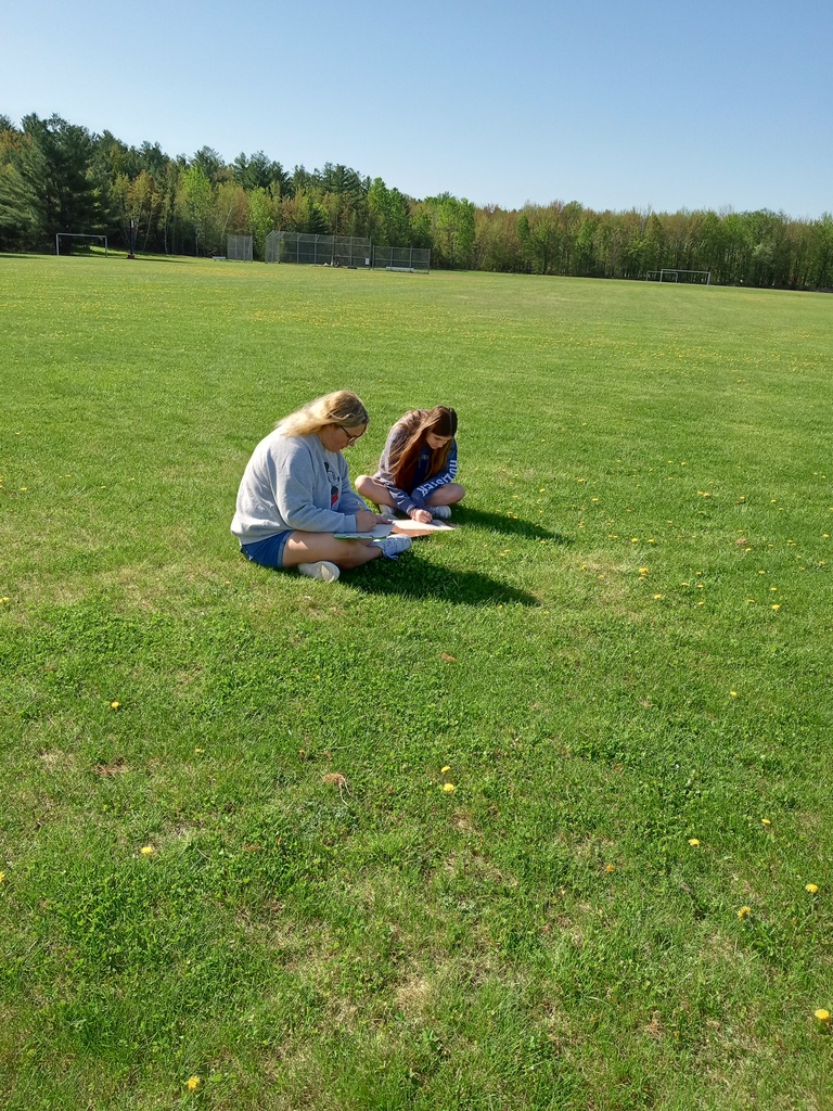 Two students sit in the grass and draw. 