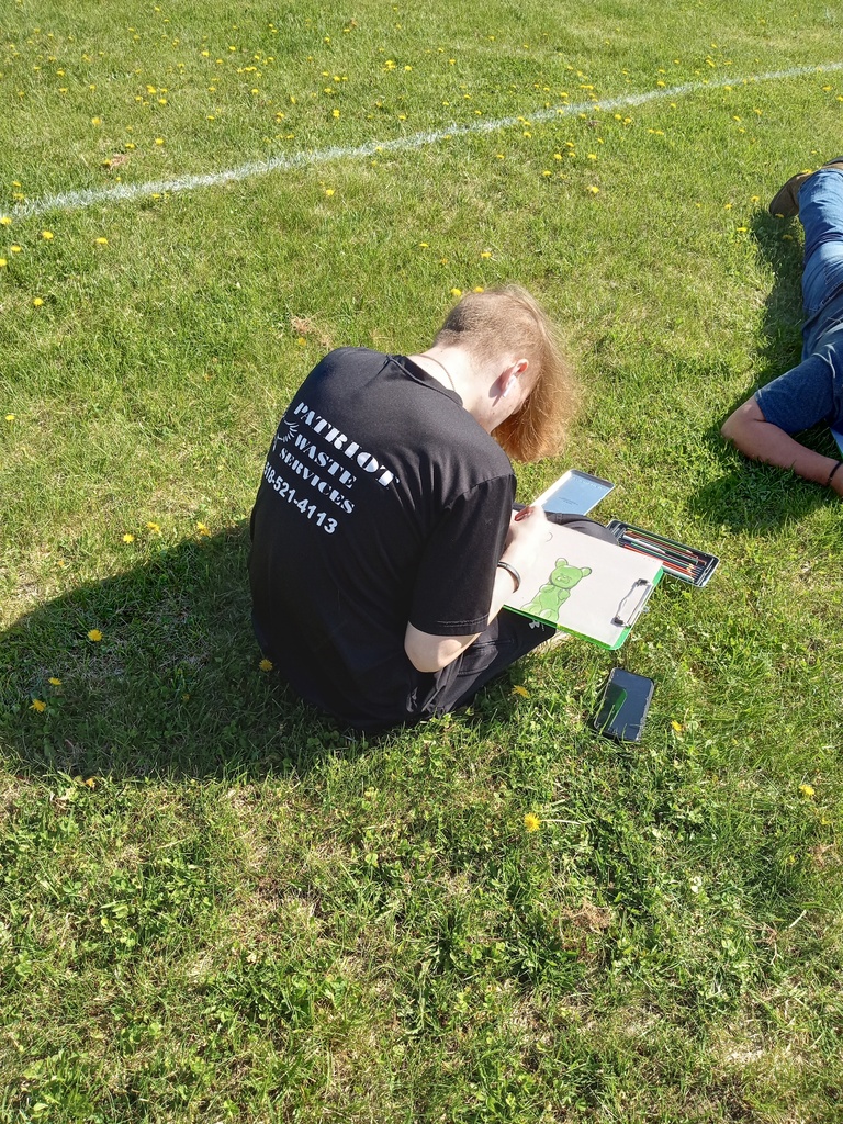 A student draws while sitting in the grass. 